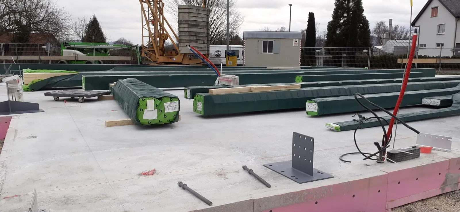 Angelieferte und noch verpackte Holzbalken liegen auf dem Fundament der zukünftigen Kletterhalle. | © DAV Sektion Hohenstaufen Göppingen