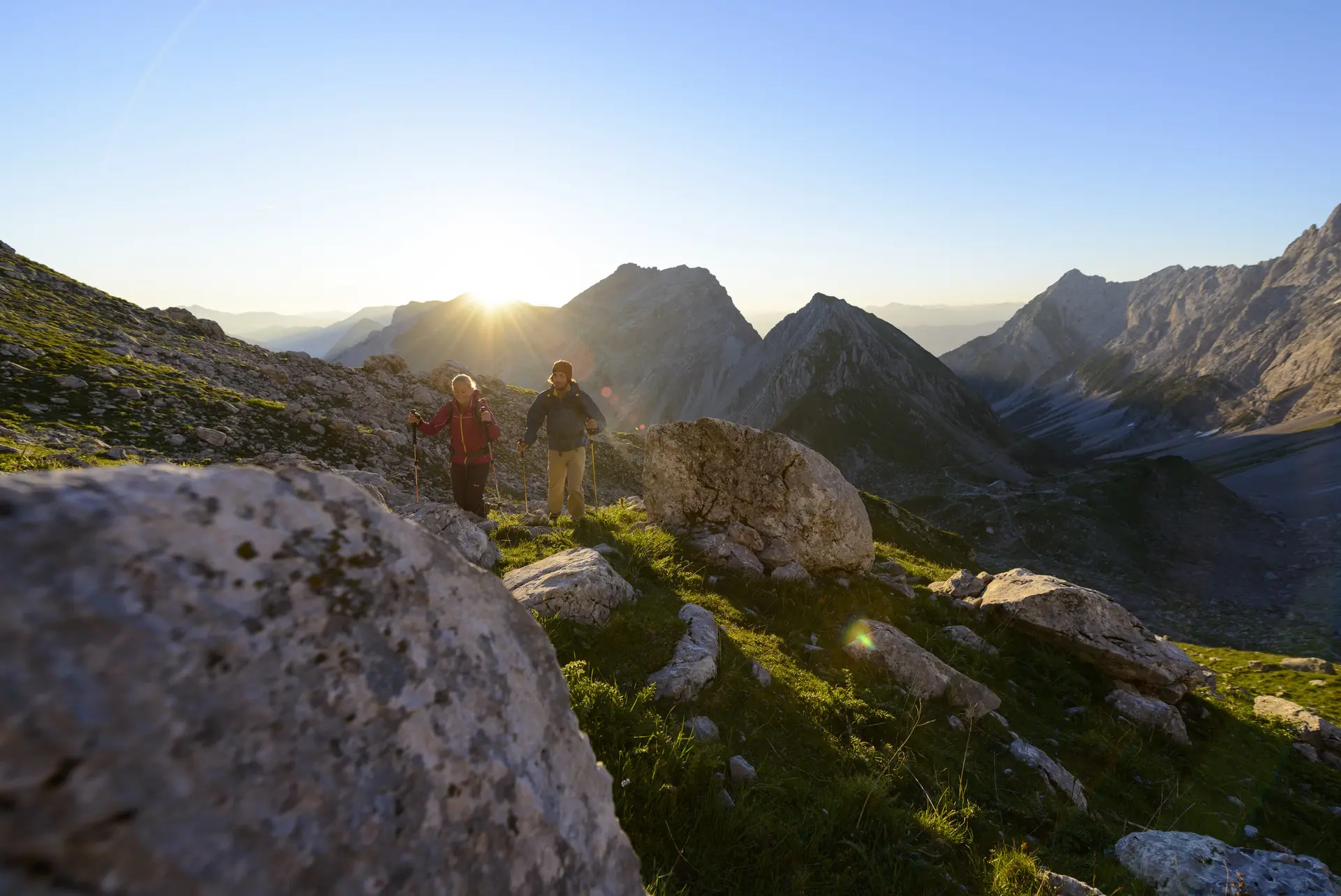 Zwei Wanderer mit Wanderstöcken in einer Berglandschaft im Licht der letzten Sonnenstrahlen | © DAV/Wolfgang Ehn