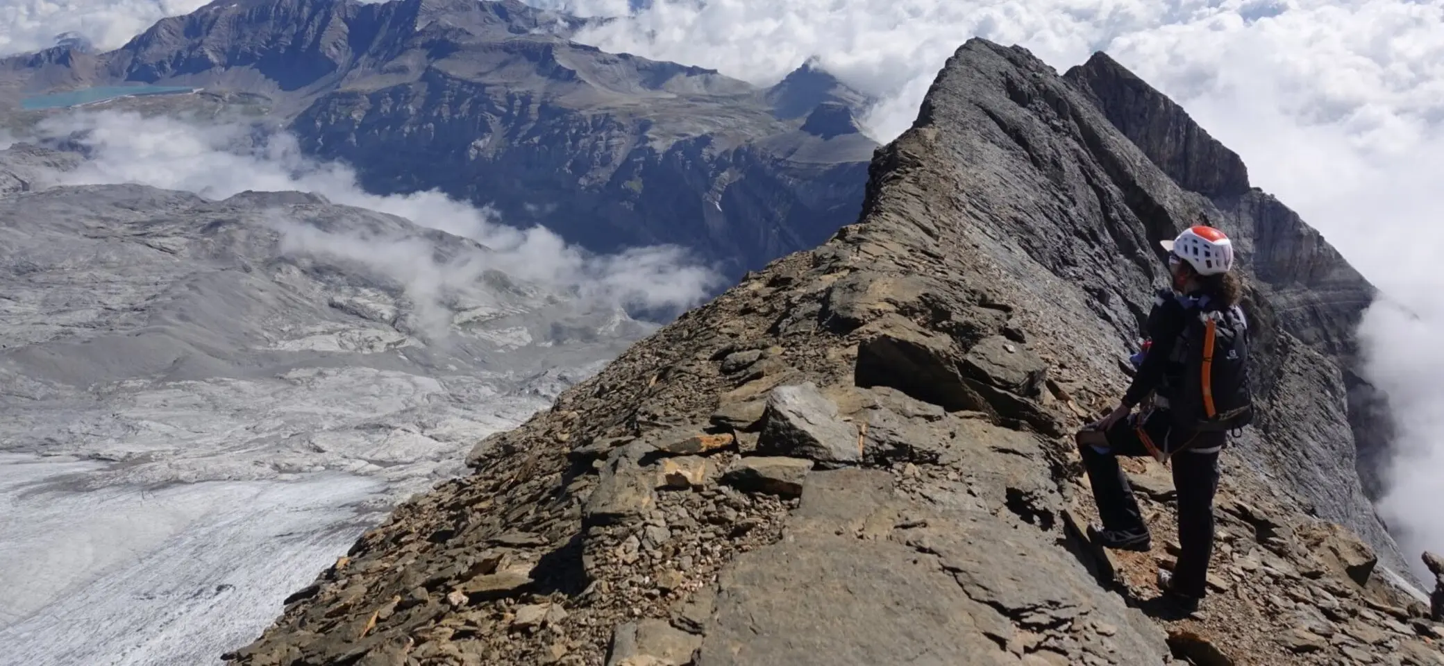 Bergsteiger steht auf dem Gipfel und blickt über die Bergkulisse mit wolkenverhangenen Tälern. | © Pete Parker Photography